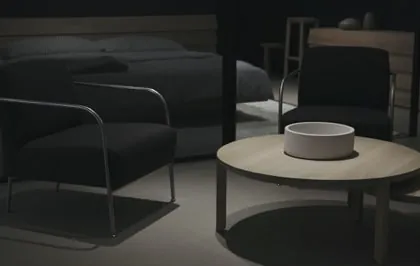 A dimly lit lounge, with dark armchairs drawn around a round wooden coffee table.