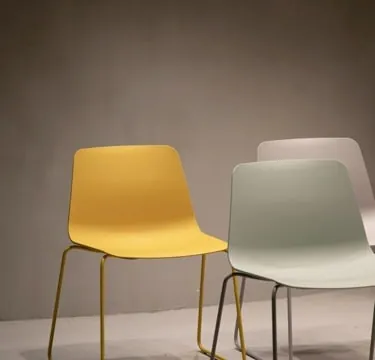 Three stacking shell chairs in mustard, sage and blush, against a warm taupe wall.