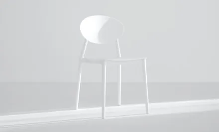 A single white chair standing alone in a bright, empty studio.